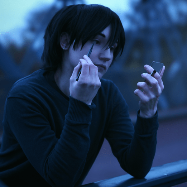 Vampir mit kurzen, schwarzen Haaren hält einen Spiegel und einen Eyeliner in den Händen