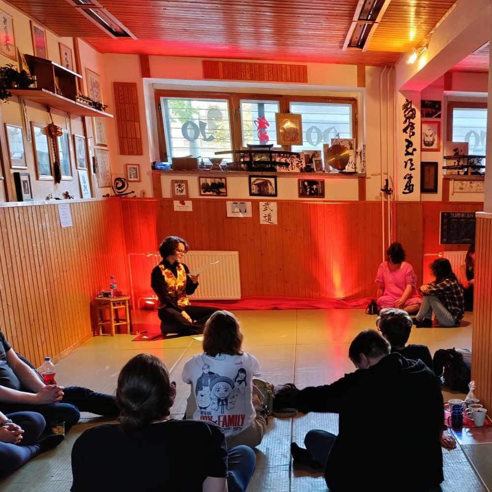 Menschen sitzen im Dojo und hören der Autorin beim Lesen zu.