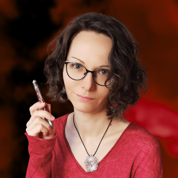 Portraitfoto der Autorin. Lächelnde Frau mit gelockten Haaren, Brille und Kuli in der Hand.